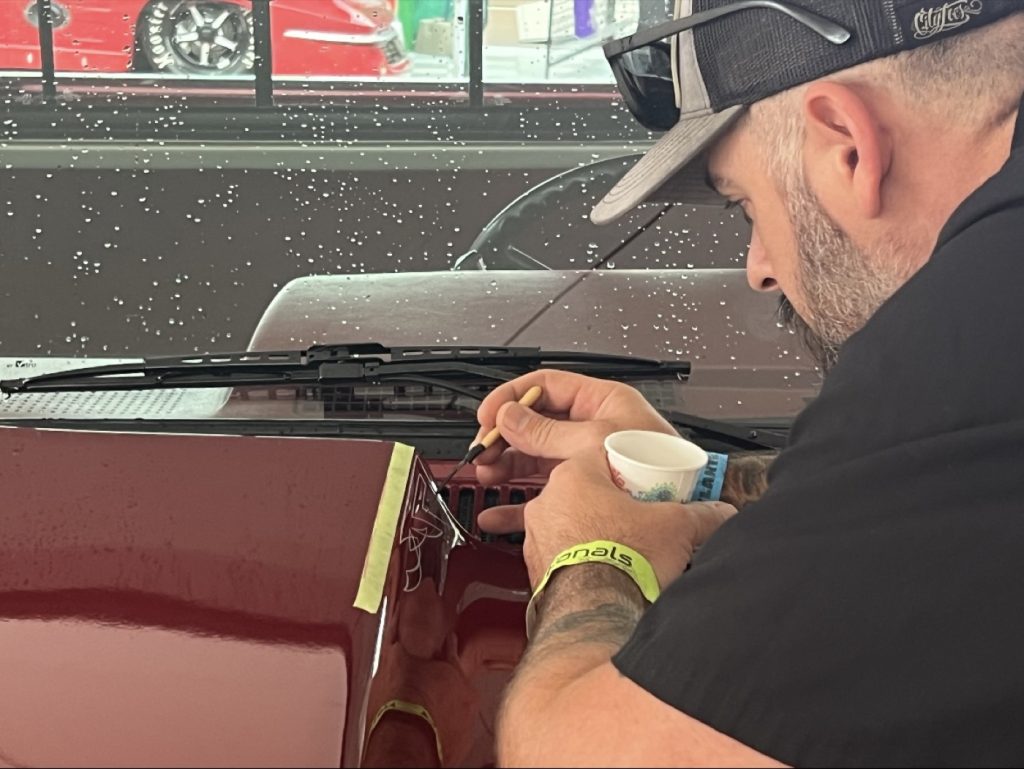 Lucas Sassman hand pinstriping a vehicle hood